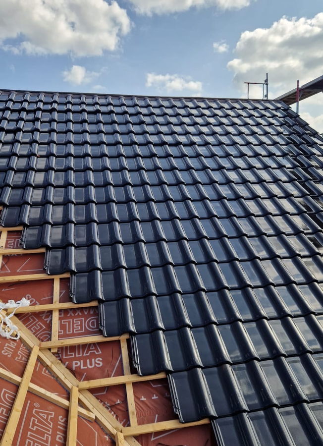 Dachfläche eines Neubaus mit glasierten dunklen Dachziegeln. Der Kehlbereich ist noch nicht eingedeckt, da dort die Kehle aus Zinkblech fehlt.
