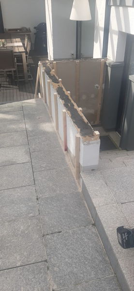 Dachlatten werden aus Haltekonstrukltion für Holzplatten an eine Mauer gedübelt.