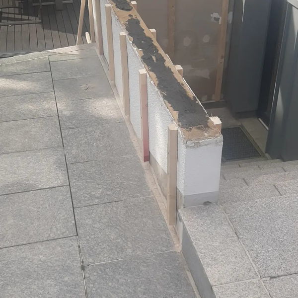 Dachlatten werden aus Haltekonstrukltion für Holzplatten an eine Mauer gedübelt.